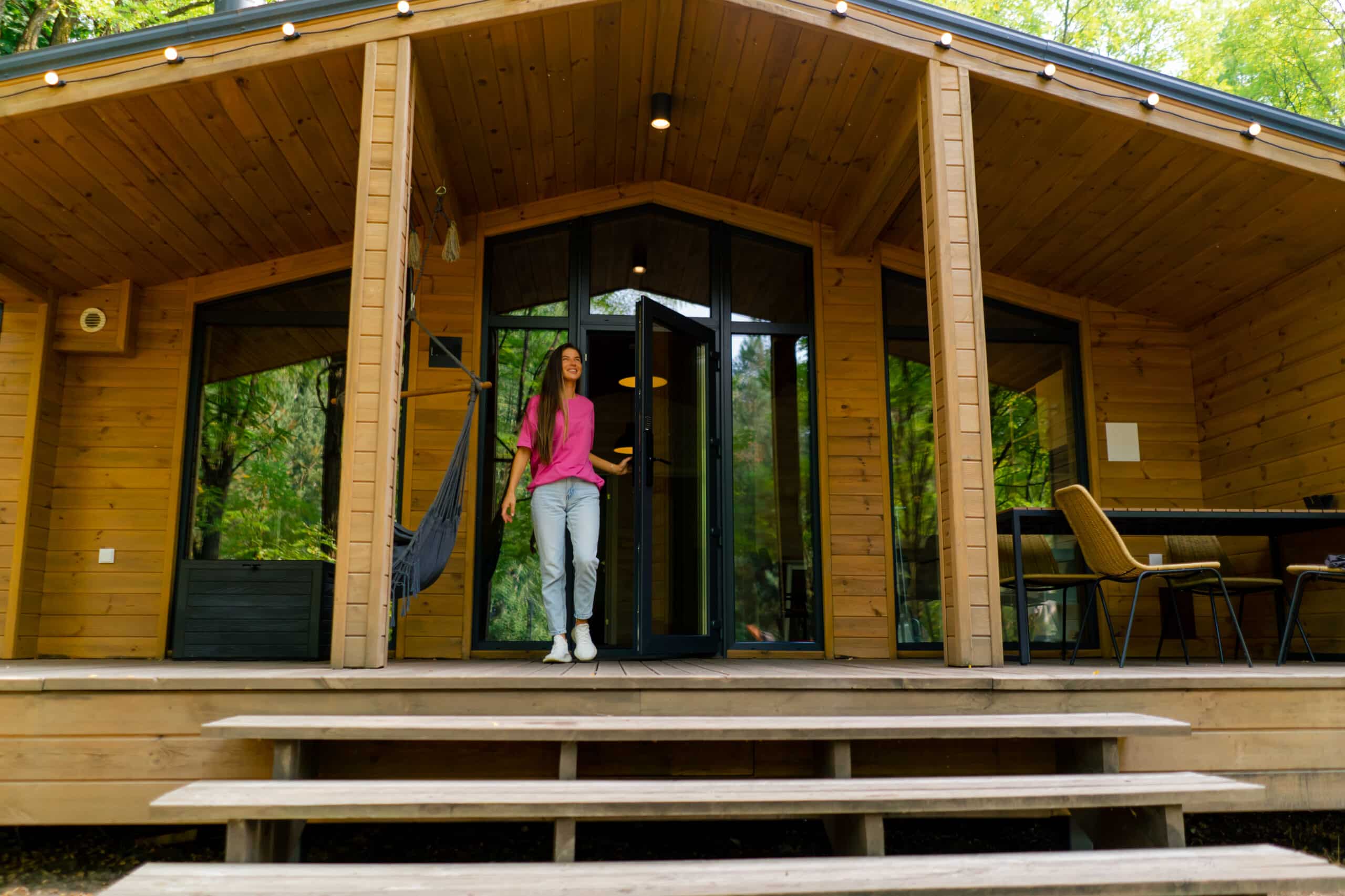 a slim smiling girl walks out in the morning on the terrace of her wooden cabin in the woods